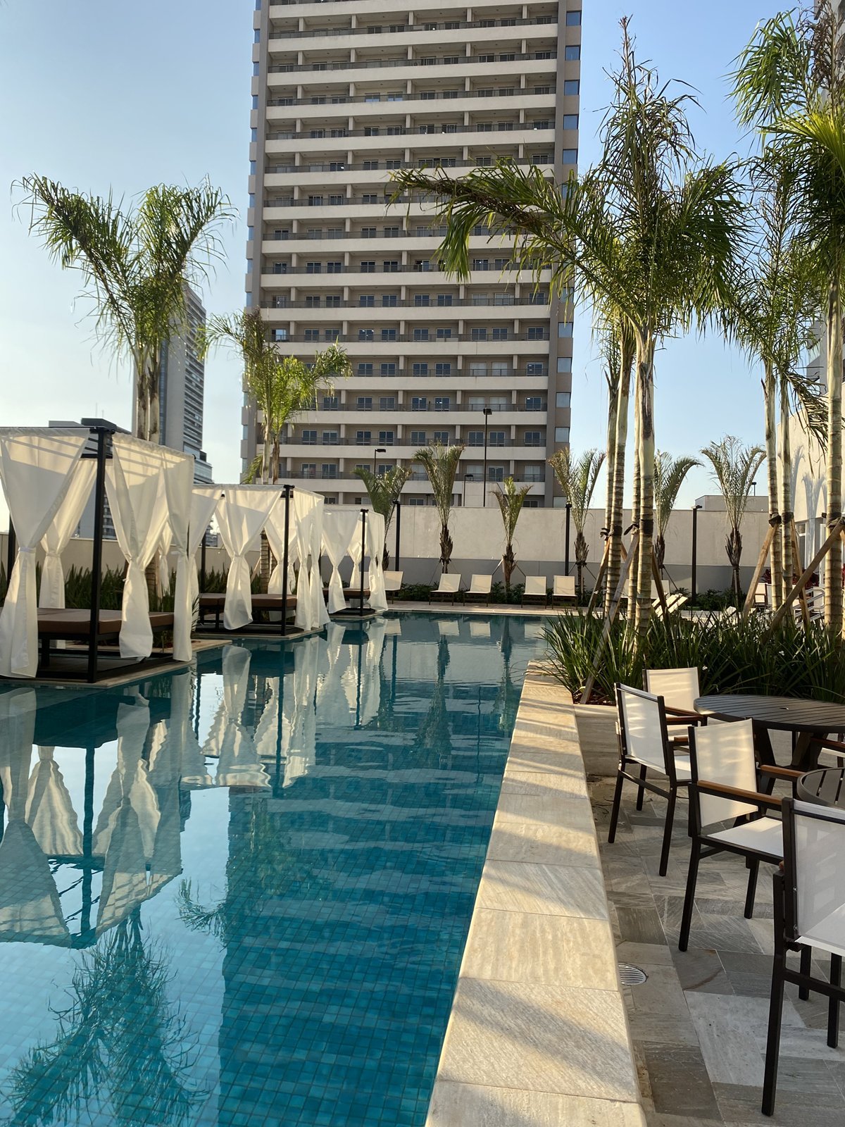 Piscina com daybeds de cortinas brancas e cadeiras sling na borda