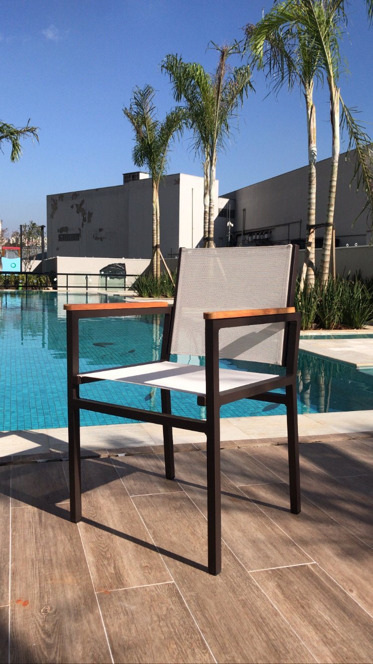 Cadeira de alumínio com tela branca e braços de madeira ao lado da piscina