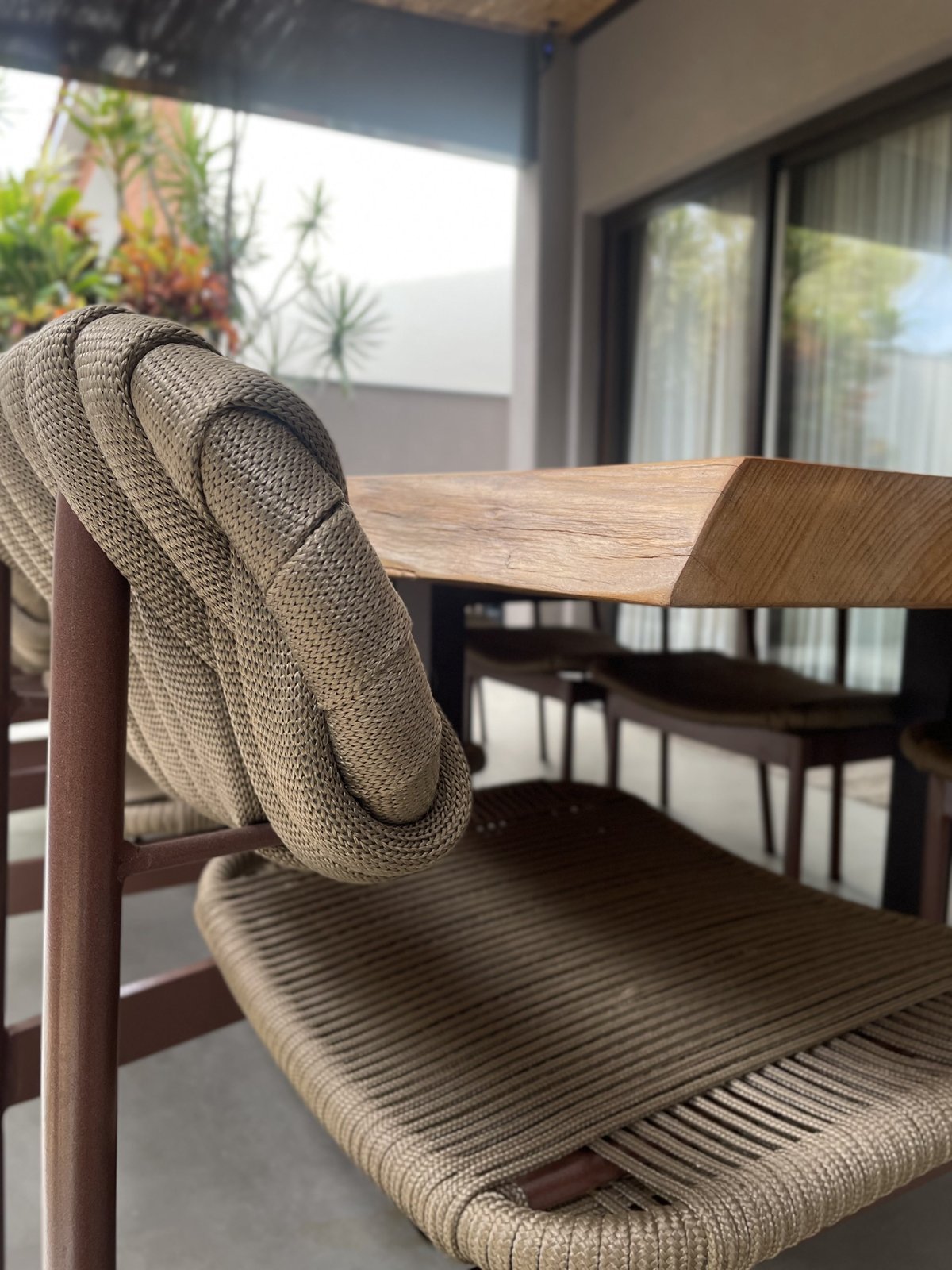 Cadeira com encosto e assento em corda trançada bege, ao lado de mesa de madeira