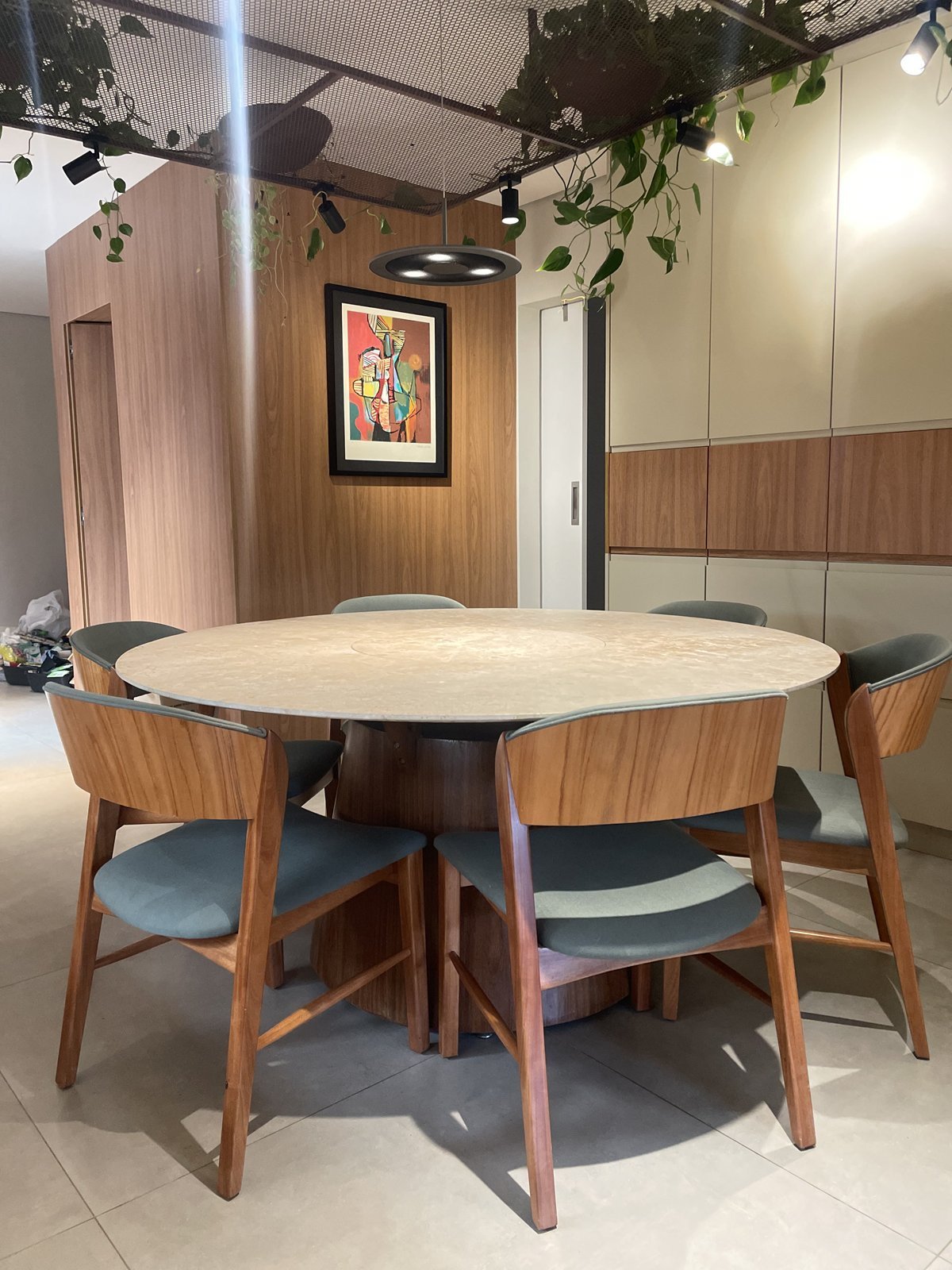 Sala de jantar com mesa redonda, cadeiras de madeira e quadro colorido