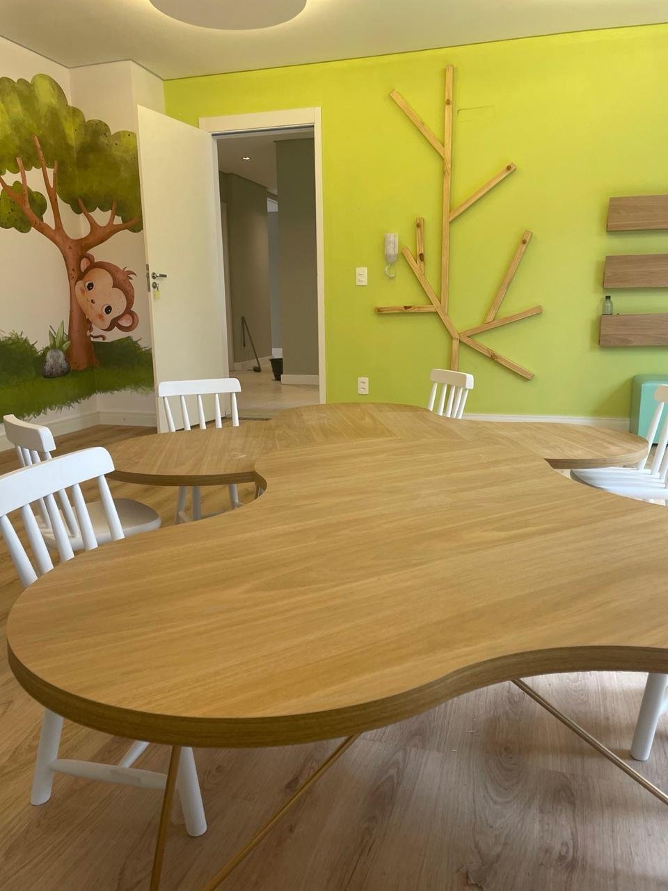 Mesa orgânica de madeira com cadeirinhas brancas numa sala infantil