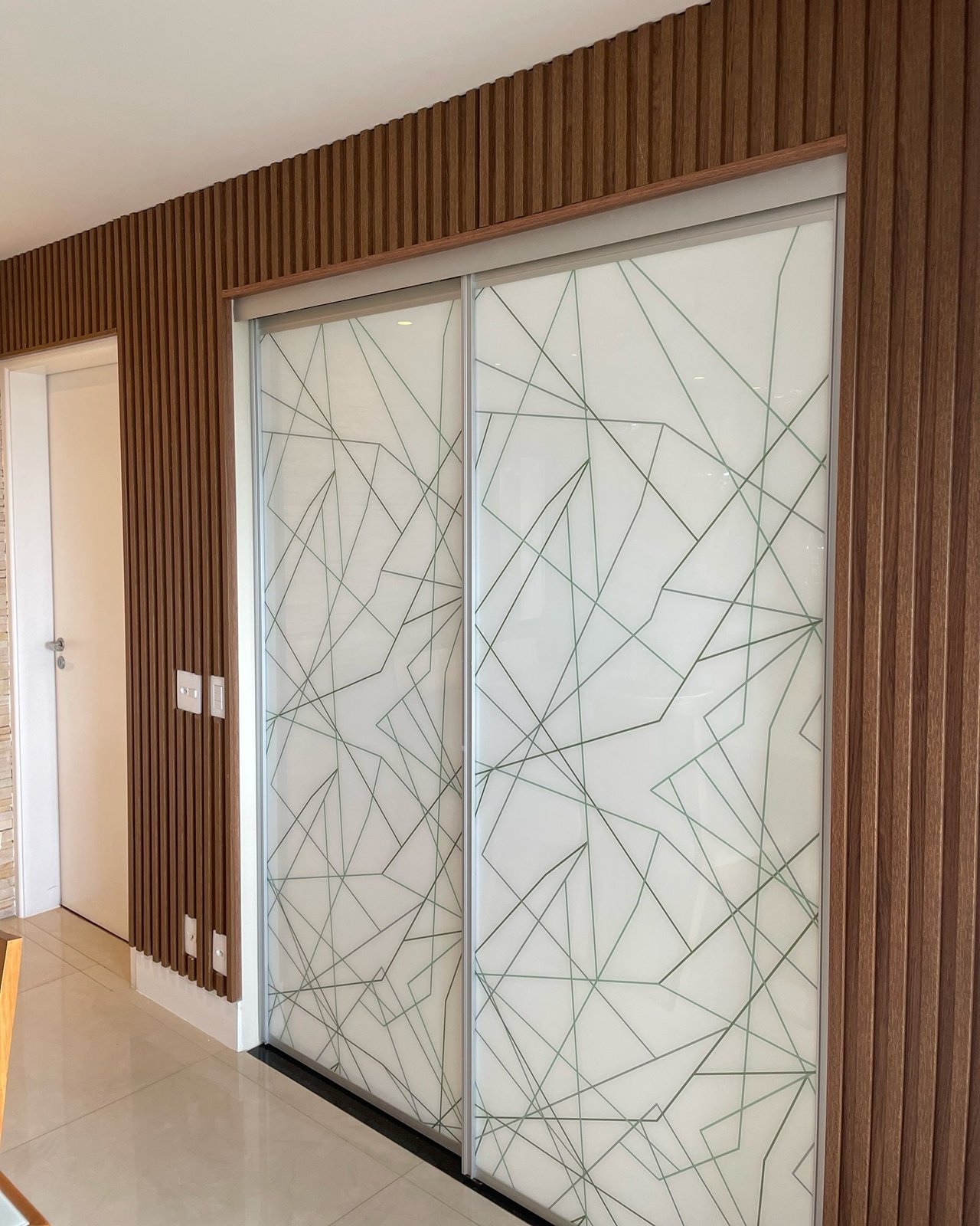 Painel ripado de madeira em toda a parede, com porta de correr em vidro decorado
