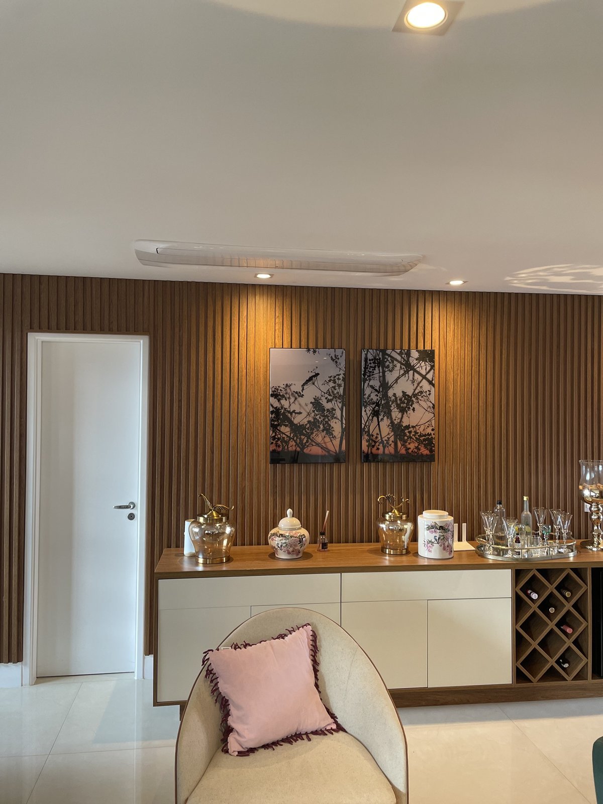 Sala com painel ripado de madeira, aparador com adega e quadros